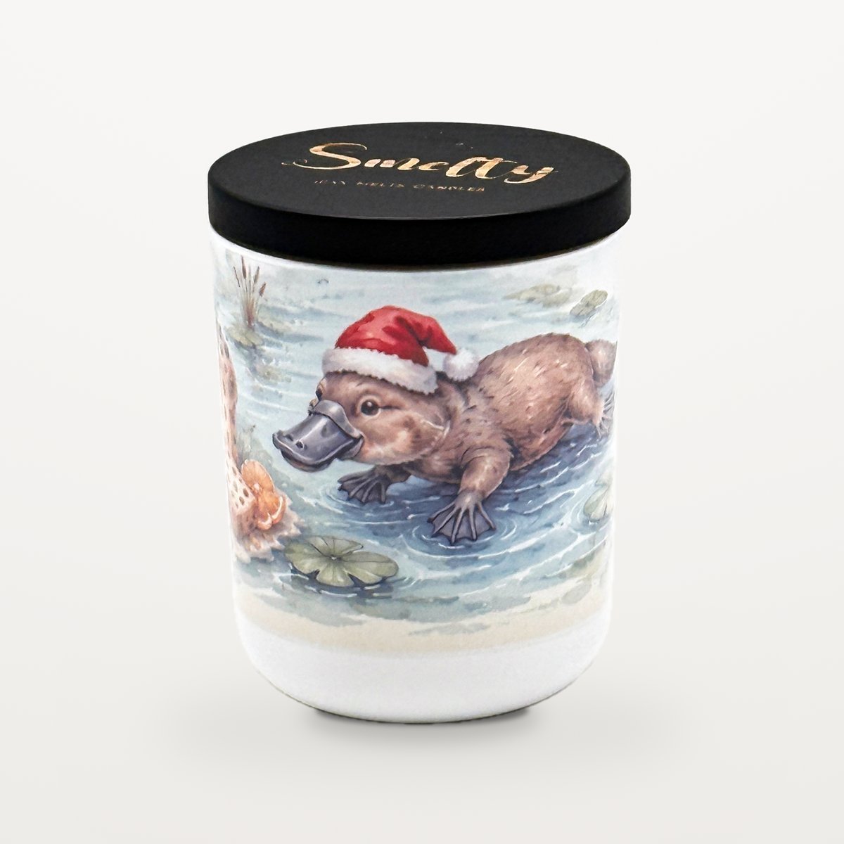 Platypus – Panettone &Amp; Fruits 1 Smelty Christmas Candle In A White Ceramic Jar With A Black Wooden Lid And Gold Smelty Logo, Printed With A Platypus In A Santa Hat Paddling In A Pond Among Lily Pads And Reeds.
